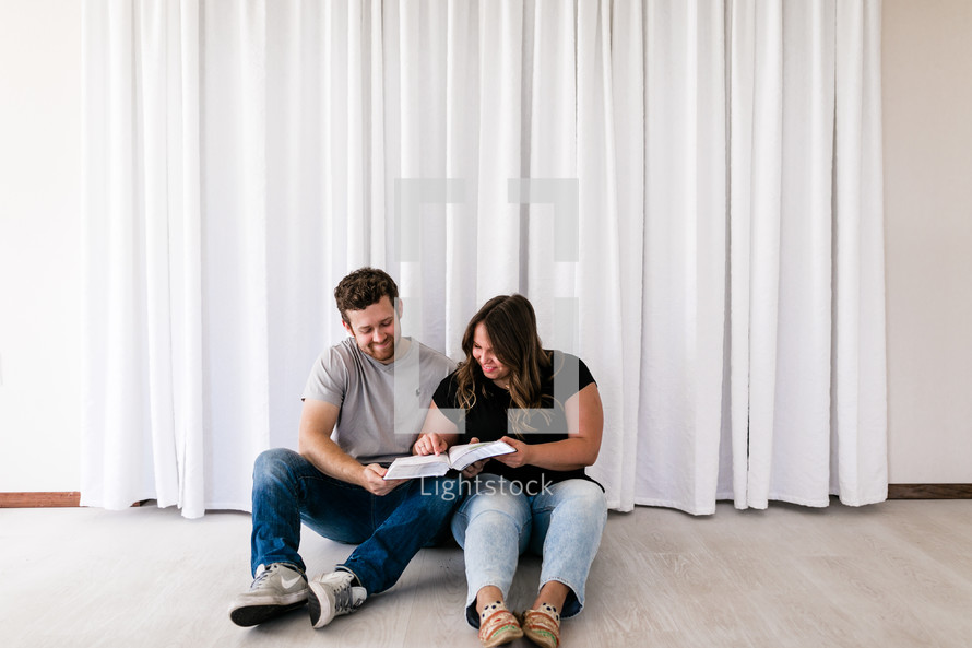 a couple sitting on the floor reading a Bible together 