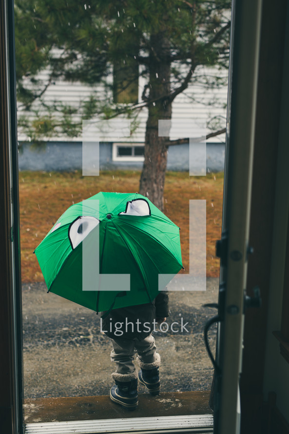 a child with an umbrella and snow boots walking out the front door