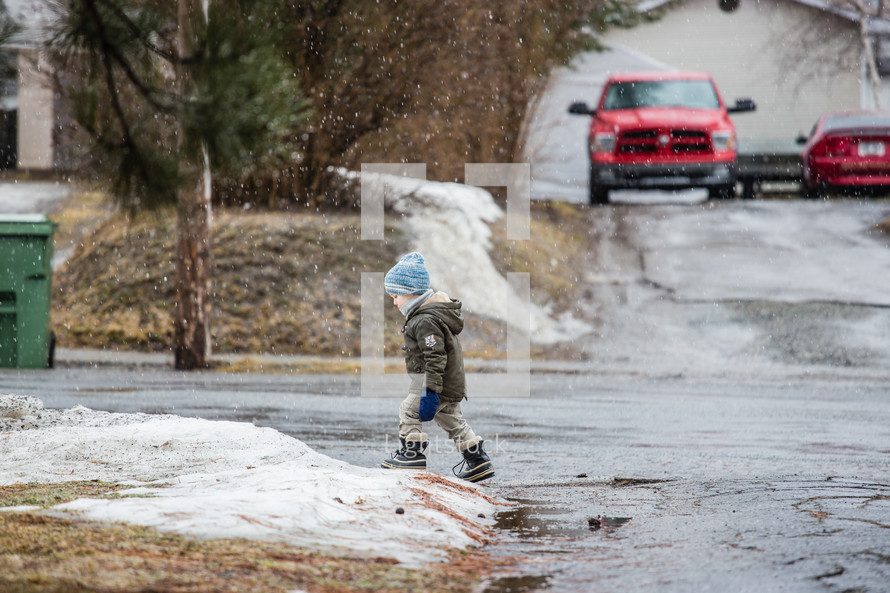 a boy child standing at the end of a driveway in falling snow 