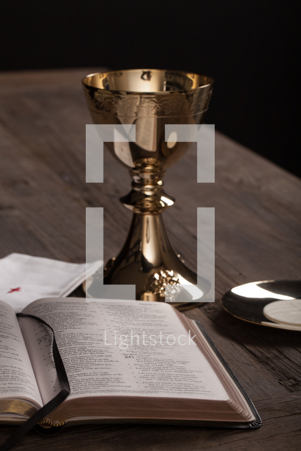 A golden communion goblet, communion wafer and an open Bible.