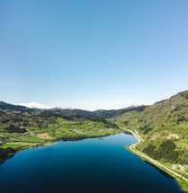 aerial view over a green valley lake surrounded by snow capped mountains 