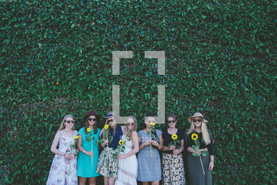 women holding sunflowers in front of an ivy wall