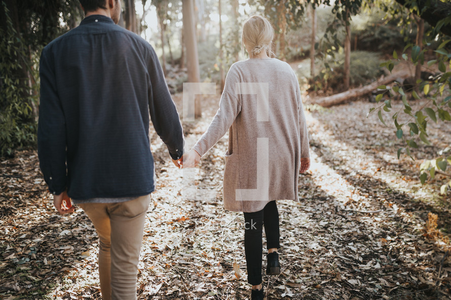 a couple walking through the woods holding hands 