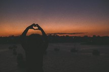 silhouette of a woman making a heart shape with her hands 