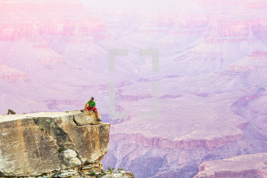 a man sitting at the edge of a cliff overlooking a canyon 