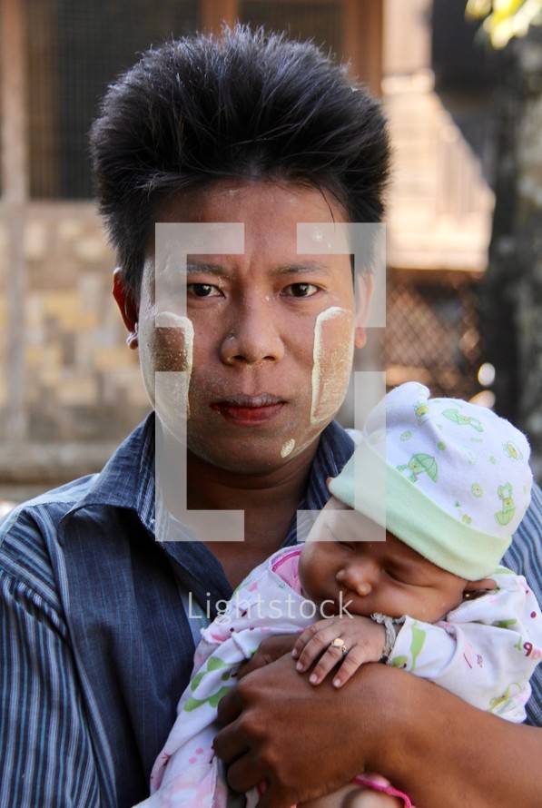a man holding an infant with traditional face paint 
