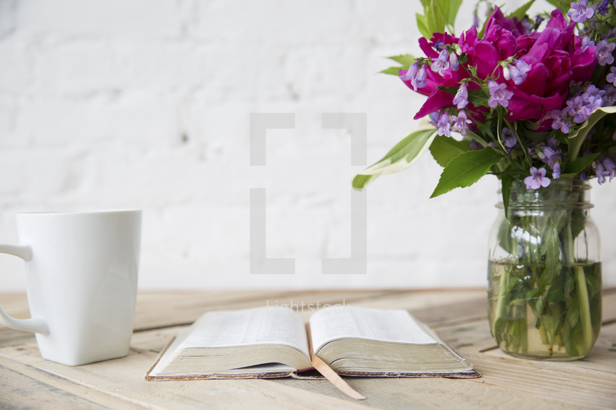 coffee mug, open Bible, and flowers in a vase on a wood table 