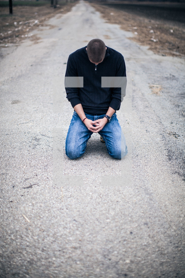 man kneeling in prayer in the middle of a road