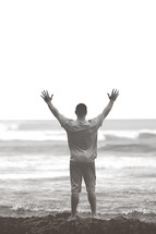 man standing with raised arms on a beach 