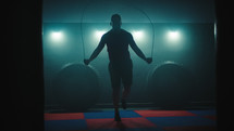 Fighter does some jump rope exercises in dark room under light