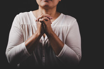 Woman with hands pressed together in prayer on a dark background