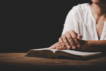 Asian woman with hands on top of her bible on a wooden table