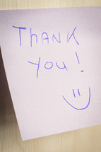 A sticky note hanging on the wall, with the text Thank You on it.