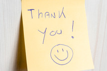 A sticky note hanging on the wall, with the text Thank You on it.