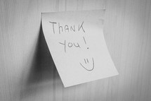 A sticky note hanging on the wall, with the text Thank You on it.