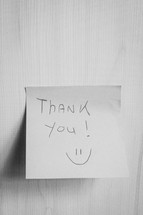 A sticky note hanging on the wall, with the text Thank You on it.