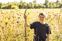 a boy with a walking stick standing in a field 