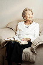Smiling elderly woman sitting on the couch reading the Bible.