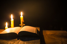 Open Bible on rustic wood table and candles