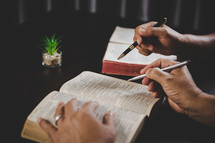 Two people studying the Bible with pens