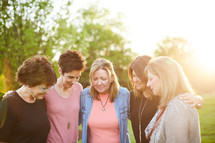 women standing in a backyard praying together 