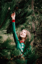 girl reaching up in pine tree
