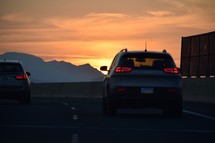 cars traveling on a freeway at sunrise under the glow of an orange sky 