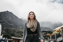 a young woman in a scarf and sweater with mountains in the background 
