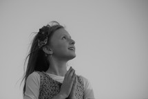 a little girl looking up to God with praying hands 