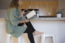 a woman in her pajamas reading in the kitchen with coffee 
