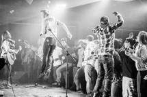 Audience rushing the stage during a concert with band jumping and playing.