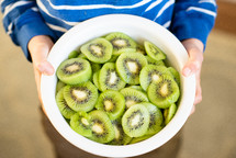 a kid holding a bowl of sliced kiwi fruit 