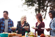 friends gathered around a table outdoors getting food in fall 