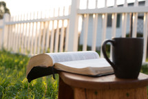 open Bible and coffee mug in a wood chair outdoors 