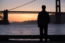 Silhouette of a man and a suspension bridge.