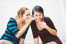 Two girls telling secrets and laughing, sitting on floor