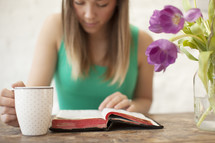 Woman with a coffee cup  reading the Bible on a wood table with tulips.