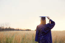 female graduate walking through a field of tall grasses 