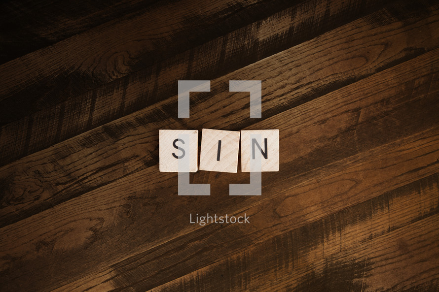 The word "sin" spelled out in scrabble letters on wooden background