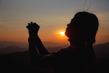 Silhouette of woman praying at sunset