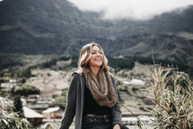 smiling woman sitting on a rock wearing a scarf and sweater 