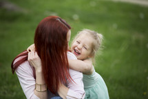 A laughing little girl with her arms around her mother.