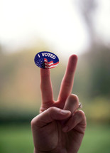 hand holding up a peace sign and a I voted sticker 