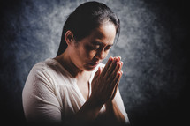 An Asian woman praying with hands folded together.