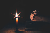 Woman hands praying on Holy Bible with candle light.