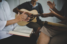 Group of people worshiping together with Bibles and a guitar