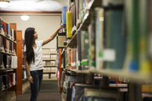 woman standing in a library looking at books on a bookshelf 