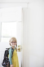 girl child with a backpack opening a door 