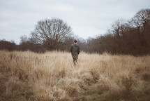a man walking through a field of tall grasses