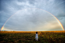 Rainbow over a wet corn field with child 